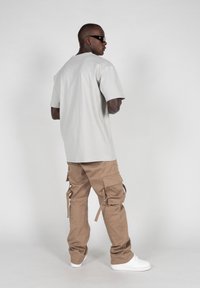 Lys grå, oversized t-skjorte, løse sandfargede cargo-bukser med sidelommer, og hvite sneakers. Modellen står med ryggen mot kameraet.