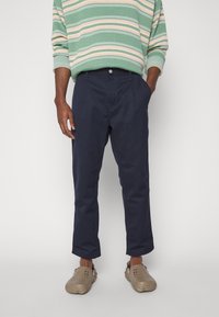 Námořnicky modré kalhoty s volnějším střihem, mají pas, kapsy a čistý vzhled. Nosit s proužkovaným zeleným a pastelovým svetrem.