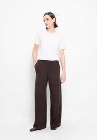 Jasnoróżowa bluzka z krótkim rękawem w połączeniu z brązowymi spodniami o szerokich nogawkach. Posiada gładki materiał, prosty krój i boczne kieszenie w spodniach.