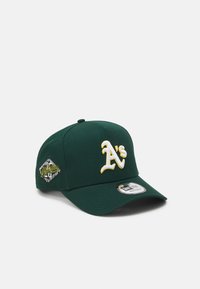 Gorra de béisbol verde con el logo bordado "A's" en blanco y amarillo. Presenta una forma estructurada y una visera curvada con una etiqueta de marca.