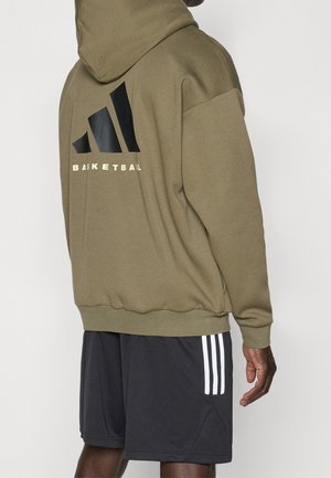 Person wearing an olive green hoodie with the word "BASKETBALL" and logo on the back, paired with black shorts with three white stripes.