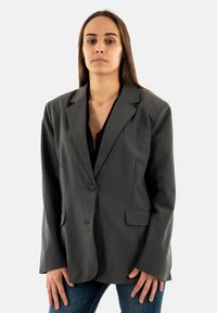 Blazer gris con un solo botón, dos bolsillos frontales y solapas de pico. Hecho de tela suave, presenta un ajuste natural y mangas largas.