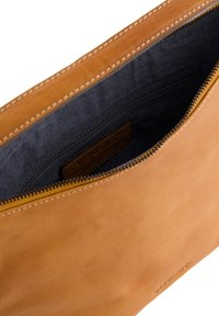 Sac en cuir tan avec une texture lisse, doté d'un intérieur marine et d'une fermeture éclair. Comprend une petite poche et une couture visible.