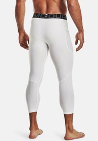 Weiße Kompressionsleggings mit einem schwarzen Unter Armour-Gummibund, ausgestattet mit einer strukturierten Oberfläche und abgerundeten Nahtdetails, entworfen für den sportlichen Einsatz.