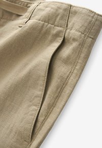Tissu en lin beige présentant une texture lisse et une poche latérale, avec une finition de couture soignée, mettant en valeur un design ajusté.