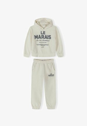 Completo felpa con cappuccio e pantaloni beige con scritta "LE MARAIS", polsini ed elastico in vita, tasche frontali, adatto per un abbigliamento casual.