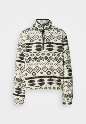Fleece-pullover med halv lynlås, der har et geometrisk sort-hvidt mønster, rundet krave og elastiske ærmekanter. Blød, struktureret overflade.