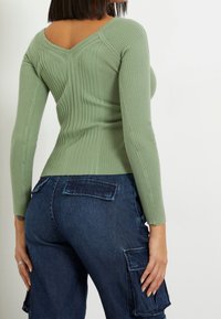 Grün gestreifter Pullover mit V-Rücken-Design und langen Ärmeln, kombiniert mit dunkelblauen Cargo-Hosen mit Aufsetztaschen.