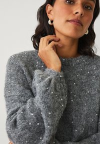 Grauer Strickpullover mit weicher Textur, verziert mit verstreuten silbernen Pailletten, mit rundem Ausschnitt und voluminösen Ärmeln.