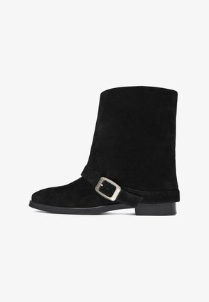 Bota de ante negra con tacón bajo y una correa con hebilla plateada en el frente, vista de lado sobre un fondo blanco.