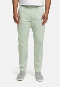 Light green cotton chinos with a straight leg and front pleats, featuring a zip fly and side pockets, paired with gray sneakers.