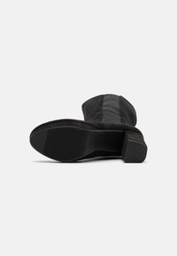 Stivale alla caviglia nero con un esterno in suede testurizzato, punta quadrata, tacco basso a blocco e pannello elastico laterale. La suola presenta un motivo rigato.