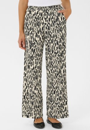Femme portant un pantalon large noir et blanc à motif avec une taille élastique, associé à des ballerines noires et un haut blanc.