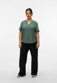 Top de manga corta y escote en V de color verde, hecho de una tela suave, combinado con pantalones de pierna ancha negros. Acentuado con zapatos de punta azul claro. Detalles mínimos.