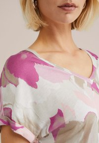 Bluza s cvjetnim uzorkom od lagane tkanine u nijansama ružičaste i bež. Ima V-izrez i uvrnute rukave, s mekanom teksturom.