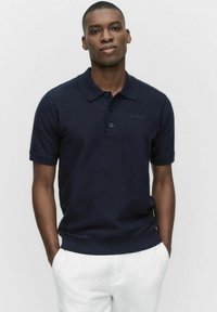 Marinblå polo skjorta i mjukt tyg, med klassisk krage, tre-knapps knäppning, korta ärmar och ribbad nederkant.