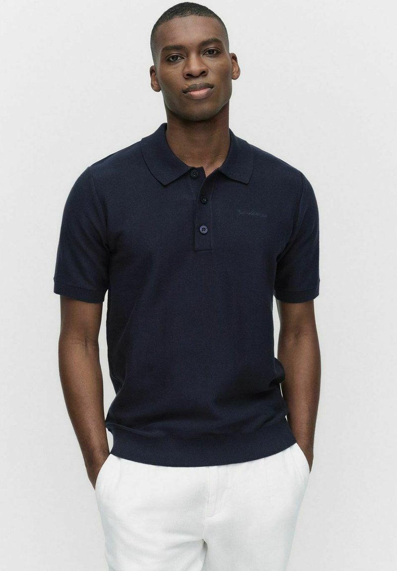 Marinblå polo skjorta i mjukt tyg, med klassisk krage, tre-knapps knäppning, korta ärmar och ribbad nederkant.