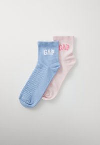 Ett par ribbade strumpor, en ljusblå med vit "GAP", en ljusrosa med rosa "GAP", ligger platt på en vit bakgrund.