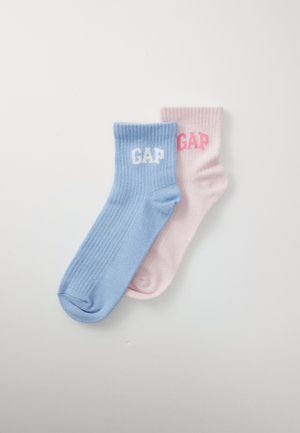 Ein Paar gerippte Socken, eine hellblaue mit weißem "GAP", eine hellrosa mit pinkem "GAP", flach auf einem weißen Hintergrund ausgelegt.