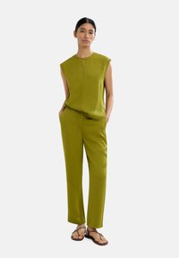 Oliwkowa, bezrękawnikowa bluzka z dekoltem w kształcie łezki, w połączeniu z dopasowanymi spodniami o prostym kroju. Gładki, lekki materiał. Płaskie sandały.