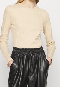 Beige ribbad långärmad topp med rund halsringning och subtila vertikala sömmar, kombinerad med svarta byxor i faux läder med elastisk midja.