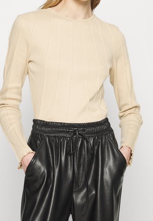 Beige geripptes Langarmshirt mit Rundhalsausschnitt und dezenten vertikalen Nähten, kombiniert mit schwarzen Jogginghosen aus Kunstleder mit elastischem Taillenbund.