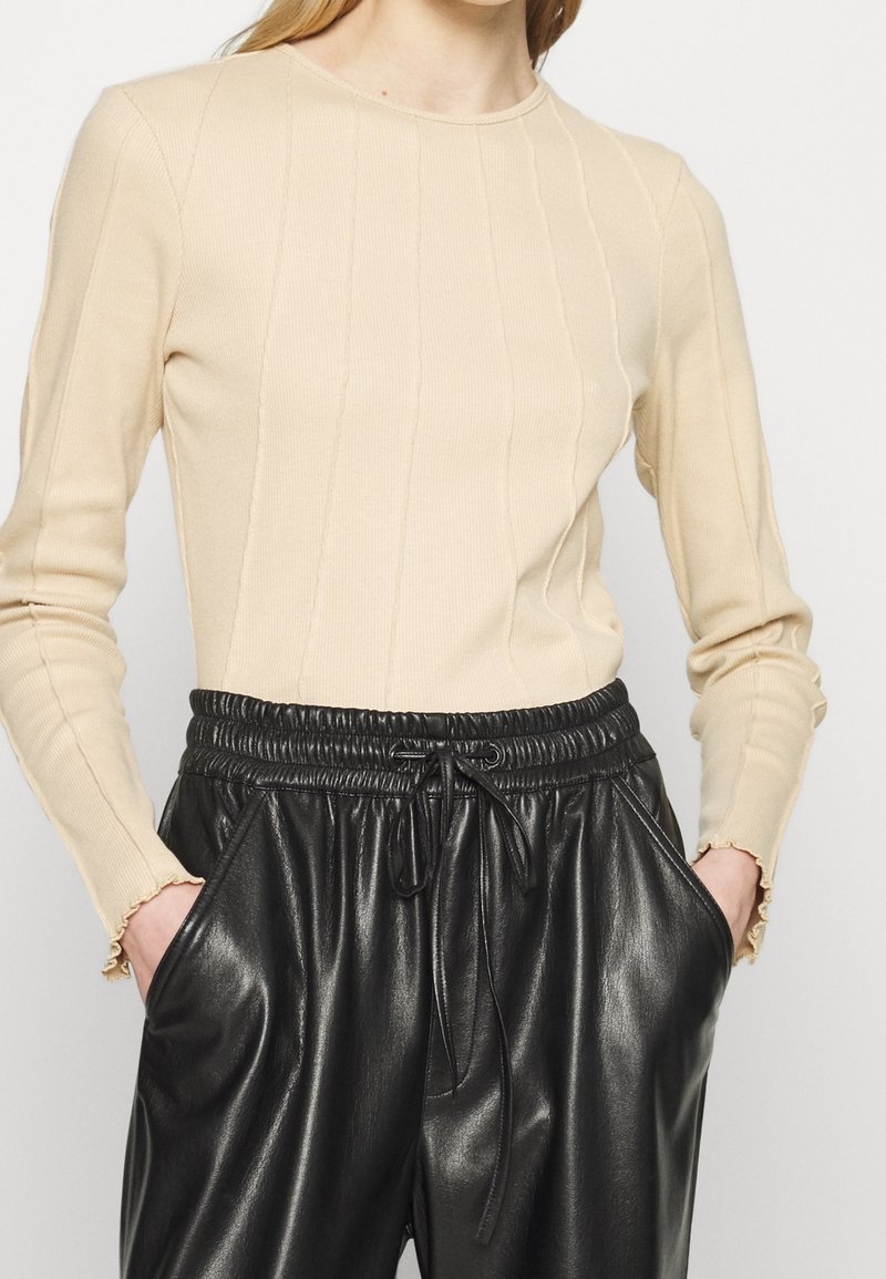 Beige ribbad långärmad topp med rund halsringning och subtila vertikala sömmar, kombinerad med svarta byxor i faux läder med elastisk midja.