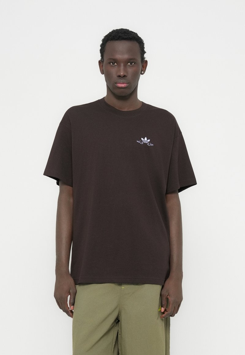 T-shirt en coton marron à manches courtes et col rond. Présente un petit logo blanc sur la poitrine. Texture lisse, coupe décontractée.