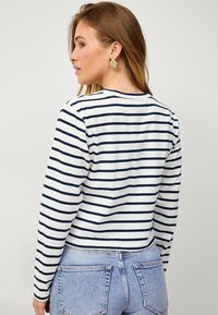 Wit langlijf-top met marineblauwe strepen, gemaakt van katoen, met een ronde nek en aansluitende pasvorm, gecombineerd met lichtdenim jeans.