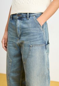 Pantaloni in denim azzurro chiaro con vestibilità comoda, dotati di grandi tasche laterali, cuciture a vista e vita media. Tessuto testurizzato.