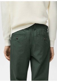 Green cotton pants with a relaxed fit, featuring an elastic waistband, back pockets with button closures, and a smooth texture.