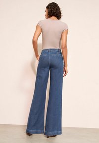 Džínsy so širokými nohavicami v stredne modrom umývaní, s vysokým pásom, pevnou tkaninou a klasicky prešitými zadnými vreckami.