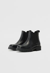 Botas de tobillo de cuero negro con paneles laterales elásticos, puntas redondeadas y suelas de goma resistentes. Diseño elegante con una lengüeta en el talón.