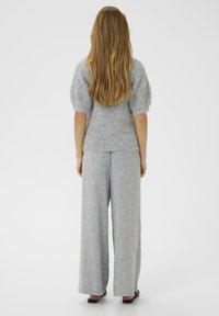 Pull en tricot gris avec des manches bouffantes, associé à un pantalon large gris clair avec un motif à chevrons discret. Chaussures plates noires.