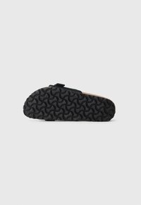 Semelle noire avec motif de grip texturé et dessus beige. Doté d'une sangle pour un maintien sécurisé. Le design est fonctionnel et épuré.