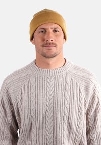 Pull en maille gris clair avec des motifs de câble surélevés, associé à un bonnet moutarde. Les deux articles présentent des finitions texturées.