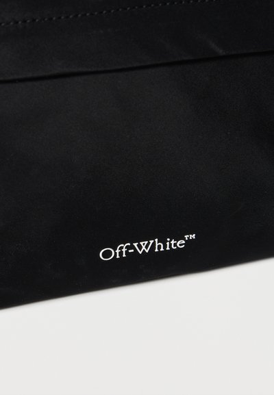 Μαύρο ύφασμα με λευκό λογότυπο "Off-White™" τυπωμένο κοντά στο κάτω άκρο πάνω σε επίπεδη επιφάνεια.