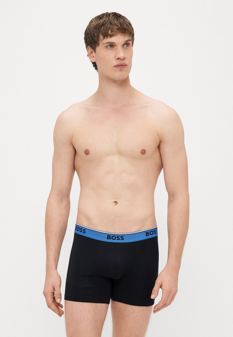 Μαύρα ανδρικά εσώρουχα-βοξέρ με μπλε λωρίδα στη μέση που φέρει το λογότυπο "BOSS". Τα εσώρουχα έχουν εφαρμοστό σχεδιασμό και λείο, ελαστικό ύφασμα.