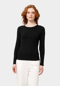 Zwarte nauwsluitende top met lange mouwen en een ronde halslijn, gemaakt van ribgebreid materiaal, gecombineerd met lichtgekleurde losse broek.