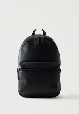 Schwarzer strukturierter Lederrucksack mit zwei Reißverschlussfächern und einem oberen Griff, minimalistisches Design auf hellem, einfarbigem Hintergrund.