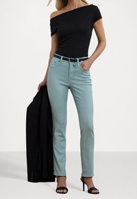 Top negro ajustado de hombros al aire combinado con vaqueros de cintura alta en azul claro, cinturón negro y sandalias de tacón alto negras, sosteniendo un blazer negro.