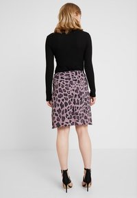 Svart ribbad långärmad topp som kombineras med en knälång lila kjol med svart leopardmönster. Svarta högklackade sandaler med remmar.