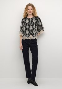 Svart topp med intrikata vita paisleymönster och en spetskant, i kombination med mörka denimjeans och svarta ankelkängor.