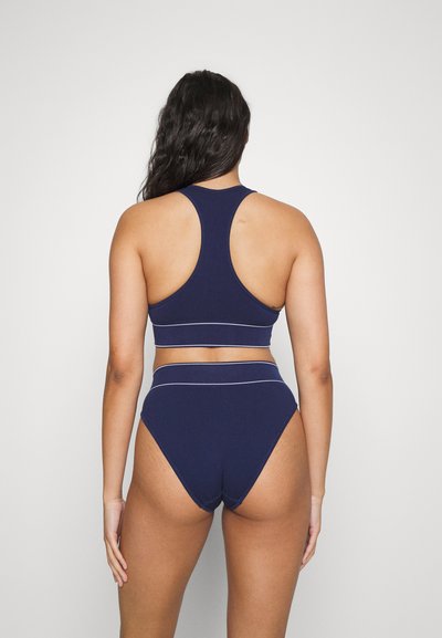 Jūras spēku ribota bikini komplekts ar racerback augšdaļu un augsto vidukļa apakšdaļu, kuram ir baltas akcentu šuves un gluda tekstūra.