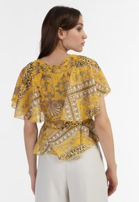 Kortærmet, gul bluse med et lagdelt design. Har en blanding af mønstre, herunder leopard- og udsmykkede motiver i brun og creme.