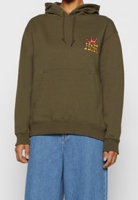 Felpa verde oliva con tasca frontale, cappuccio con coulisse e logo ricamato multicolore sul petto. Materiale in pile morbido.