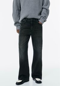 Jeans flare in denim nero con un leggero sbiadimento, design a cinque tasche e vita classica. Abbinati a un maglione grigio a coste e scarpe nere.