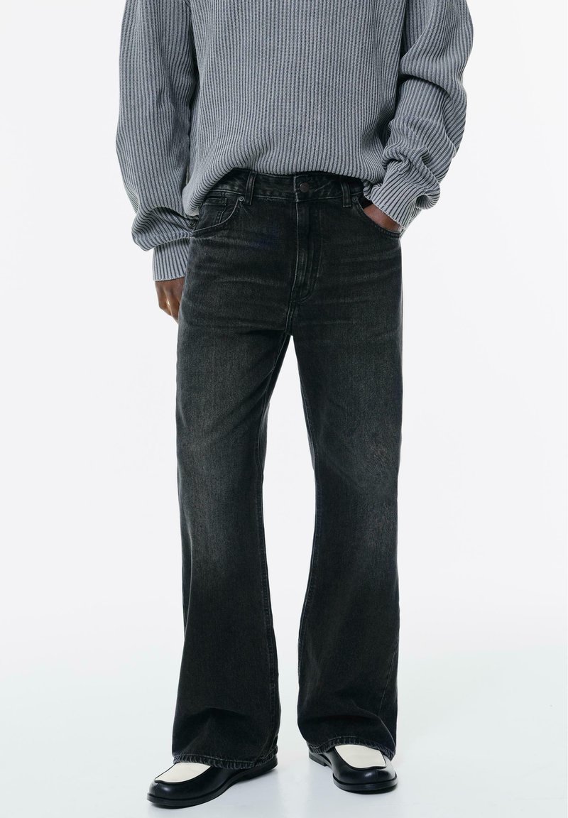 Jeans flare in denim nero con un leggero sbiadimento, design a cinque tasche e vita classica. Abbinati a un maglione grigio a coste e scarpe nere.