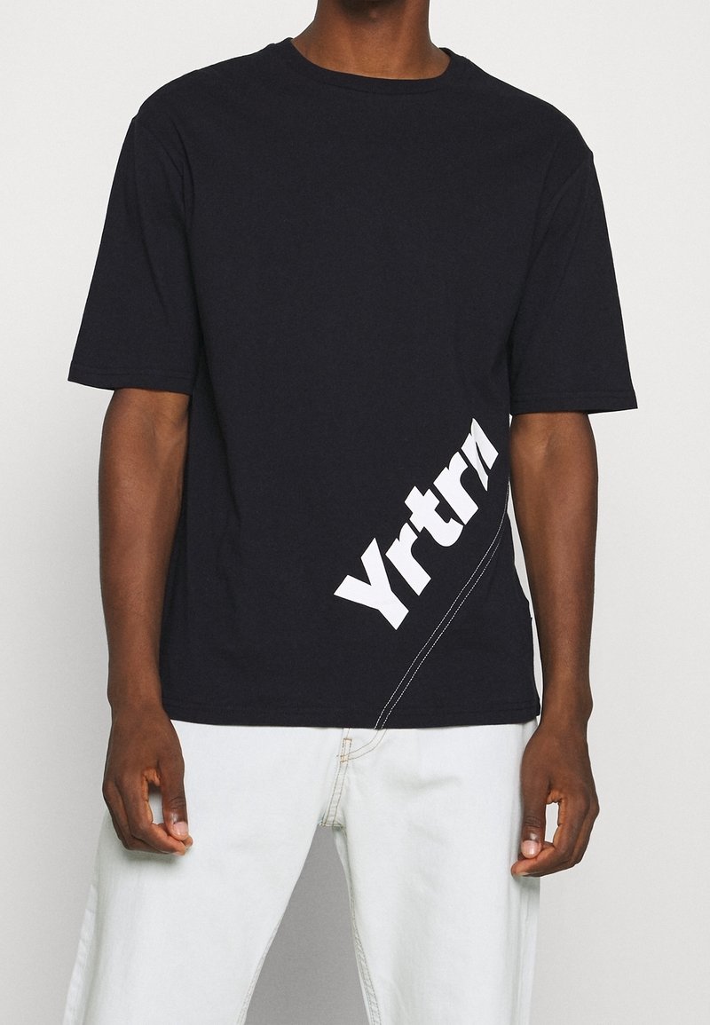 Černé bavlněné tričko s krátkým rukávem, se šikmým bílým logem "Yrtrn" a jemným švem podél lemu.