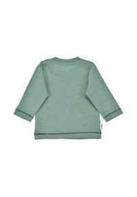 Camicia a maniche lunghe di un morbido verde menta, con collo tondo, dettaglio di bottoni sulle spalle laterali e cuciture a contrasto nere lungo le maniche e l'orlo.